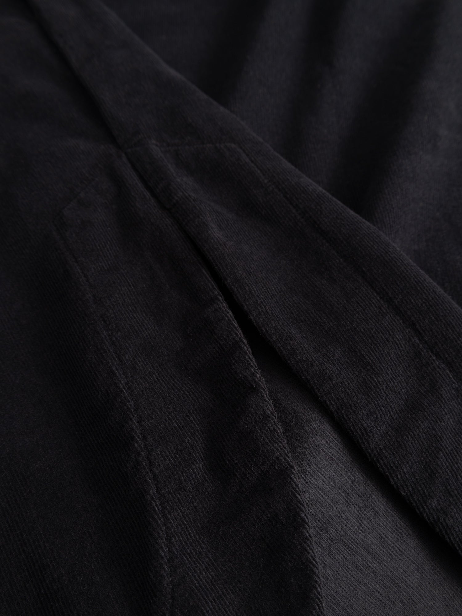 Alternate detail close-up of the Black Crane Painter Dress focusing on the curved hem and side slit detail in dark navy corduroy.