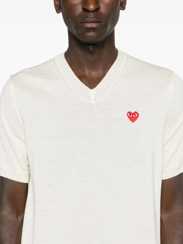 Close-up front view of a male model wearing the Comme des Garçons Play Unisex V-Neck Sweater Short-Sleeve in off white, highlighting the V-neck design, soft wool texture, and relaxed fit.