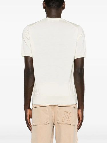 Back view of a male model wearing the Comme des Garçons Play Unisex V-Neck Sweater Short-Sleeve in off white, showing the simple unisex silhouette and short-sleeve wool finish.