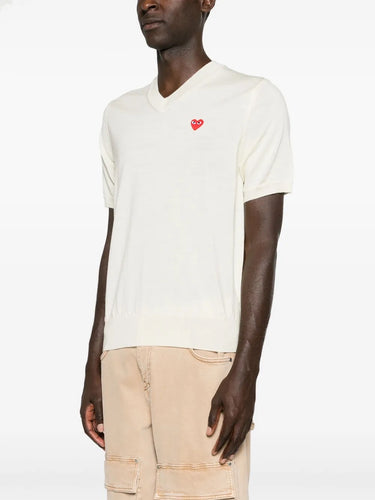 Front-side view of a male model wearing the Comme des Garçons Play Unisex V-Neck Sweater Short-Sleeve in off white, emphasizing the V-neck cut, short sleeves, and lightweight wool drape.