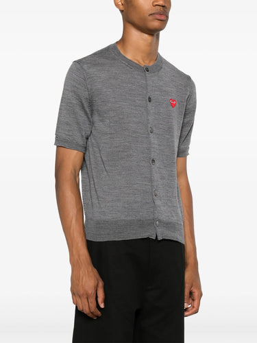 Side view of male model wearing the short-sleeve cardigan with a red heart logo from Comme des Garcons Play on a white background