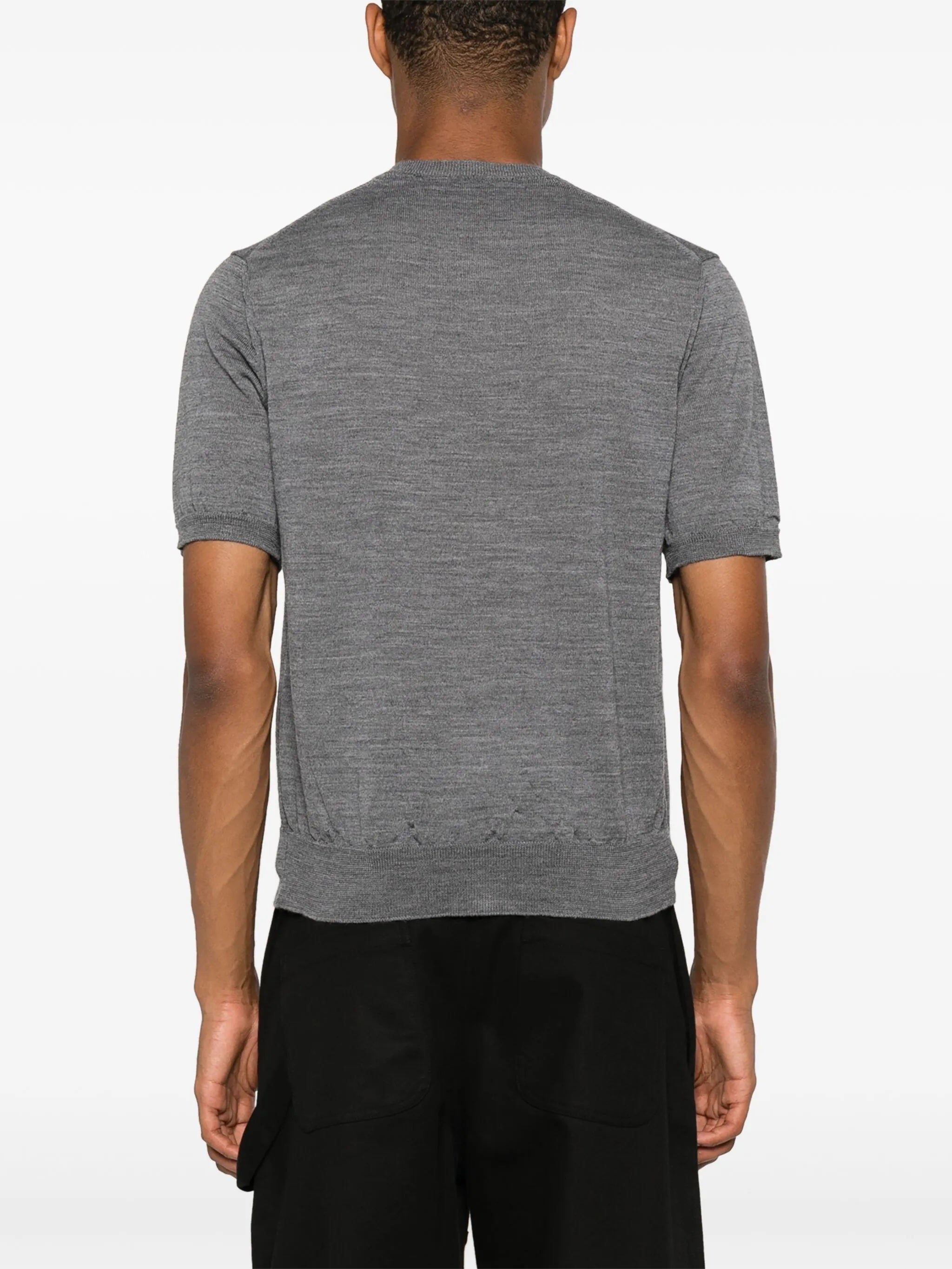Back view of male model wearing the short-sleeve cardigan with a red heart logo from Comme des Garcons Play on a white background