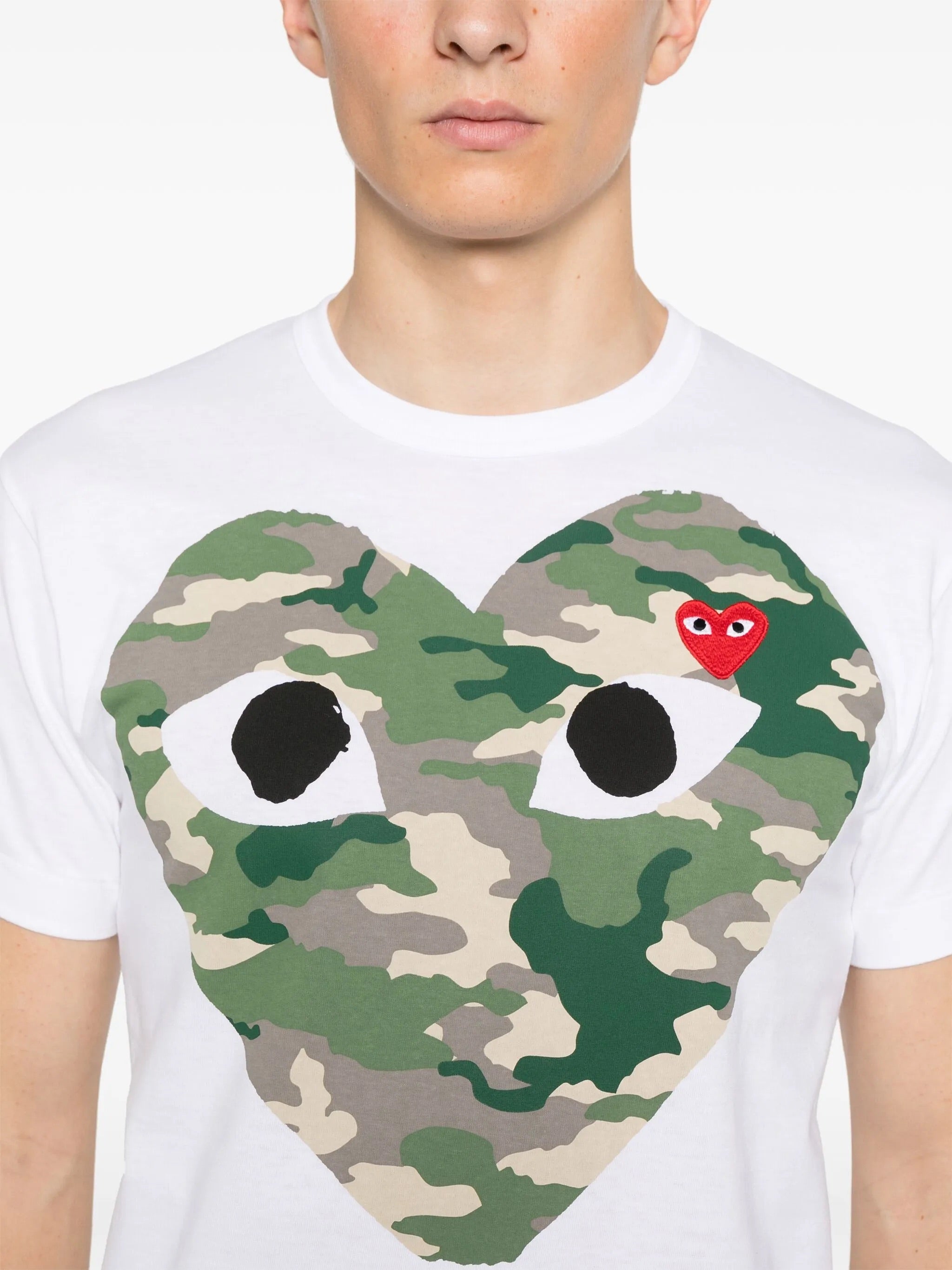 Close-up of Comme des Garçons Play white T-shirt showing camouflage heart print and red embroidered heart logo on chest