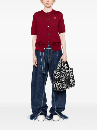 Person wearing the red short-sleeve cardigan with a red heart logo from Comme des Garcons Play on a white background