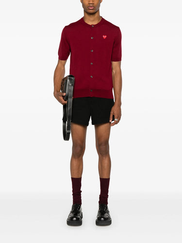 Male model wearing the red short-sleeve cardigan with a red heart logo from Comme des Garcons Play on a white background