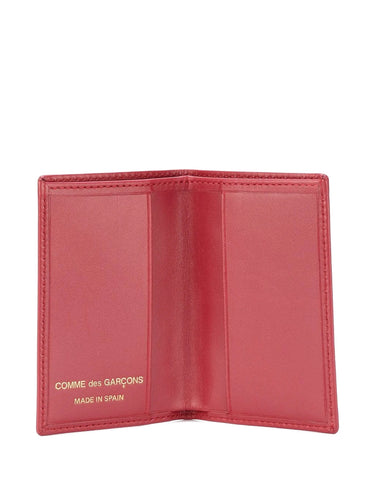 Red wallet with 'Comme des Garcons' branding on a white background