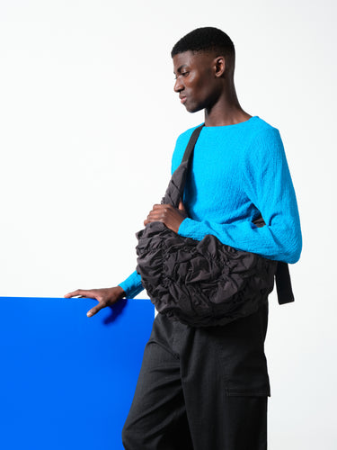Male model wearing Côte&Ciel Hyco S Otra Gathered crossbody bag in black, demonstrating ergonomic sculptural fit across the body and textured ruched nylon.