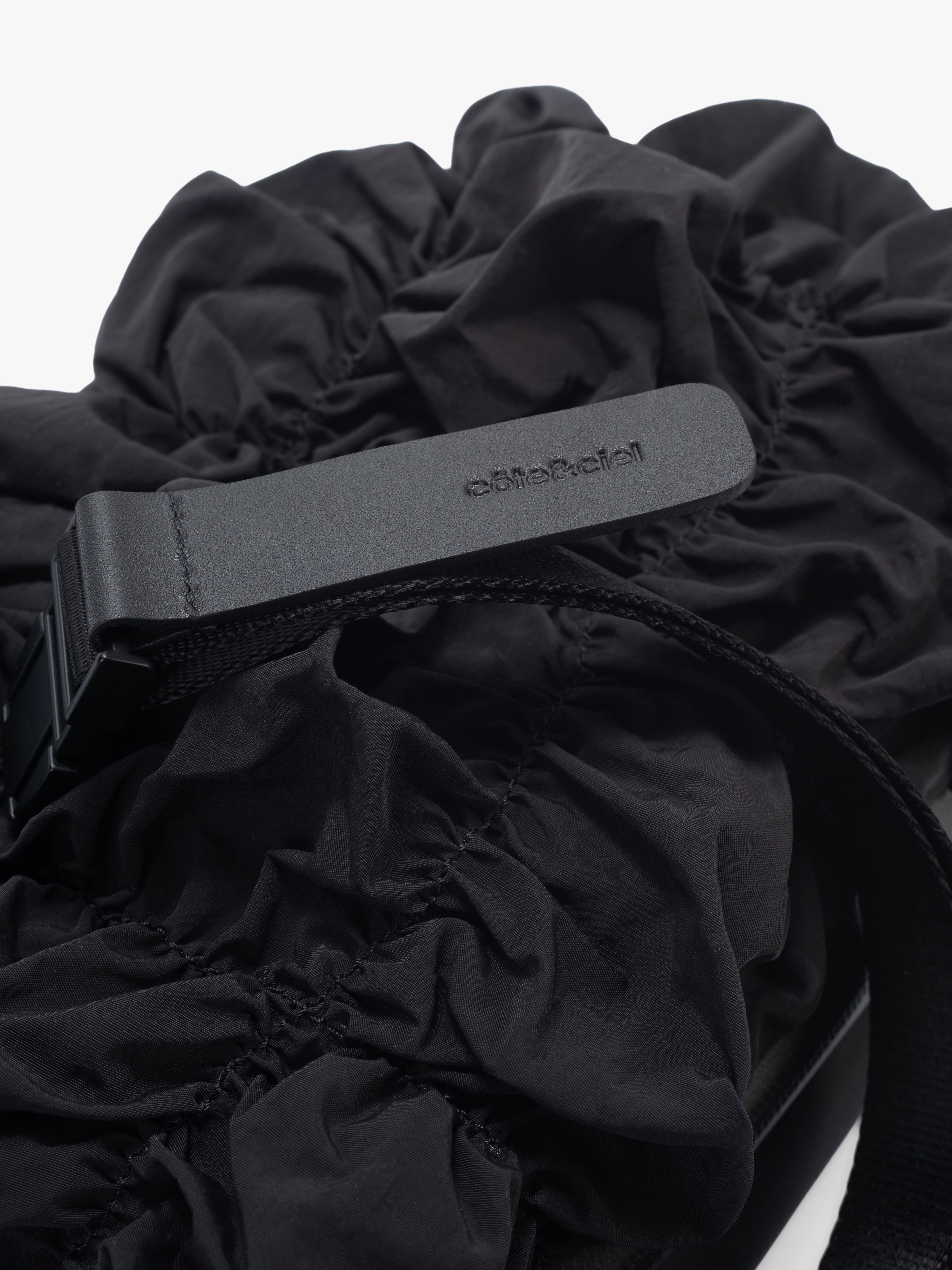 Closeup of Côte&Ciel Neva Gathered black crossbody bag, highlighting leather accent detail and ruched nylon texture.