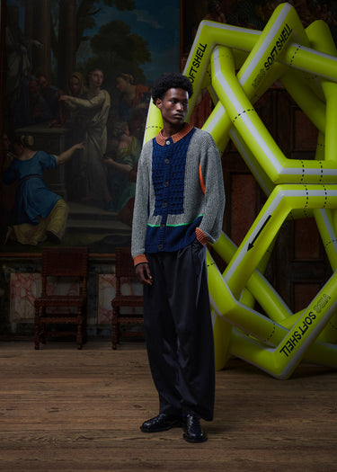 Male model wearing the Abundance Cardigan from the front, showing the unisex block design in black, white, and navy with orange accents, long sleeves, and buttoned front
