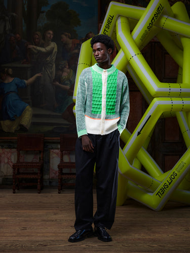 Front view of the male model wearing the Abundance Cardigan from Henrik Vibskov Spring/Summer 2026 Studio Collection, displaying the unisex block design in green, grey, and navy with beige details and buttoned front.