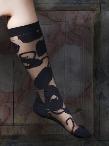 Close-up of a leg wearing the Amulet Long Socks in Black Amulets from Henrik Vibskov Spring/Summer 2026 Studio Collection, highlighting the tight fit and thick black patterned design.