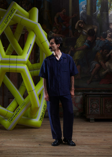 Front view of the male model wearing the Artist Pants in navy from Henrik Vibskov Spring/Summer 2026 Studio Collection, showing the straight-leg fit, front closure, and side pockets.