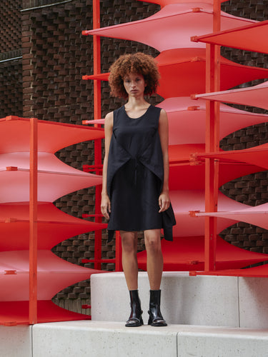 Model wearing Henrik Vibskov Beetle Dress in black, front tie styling, sleeveless sculptural silhouette, showing contemporary SS26 design.