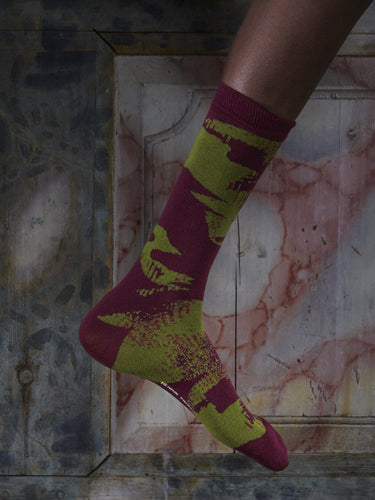 Close-up of a leg wearing the Bubble Wrap Socks in Wine Bubble from Henrik Vibskov Spring/Summer 2026 Studio Collection, highlighting the bordeaux colour and green bubble-pattern accents.