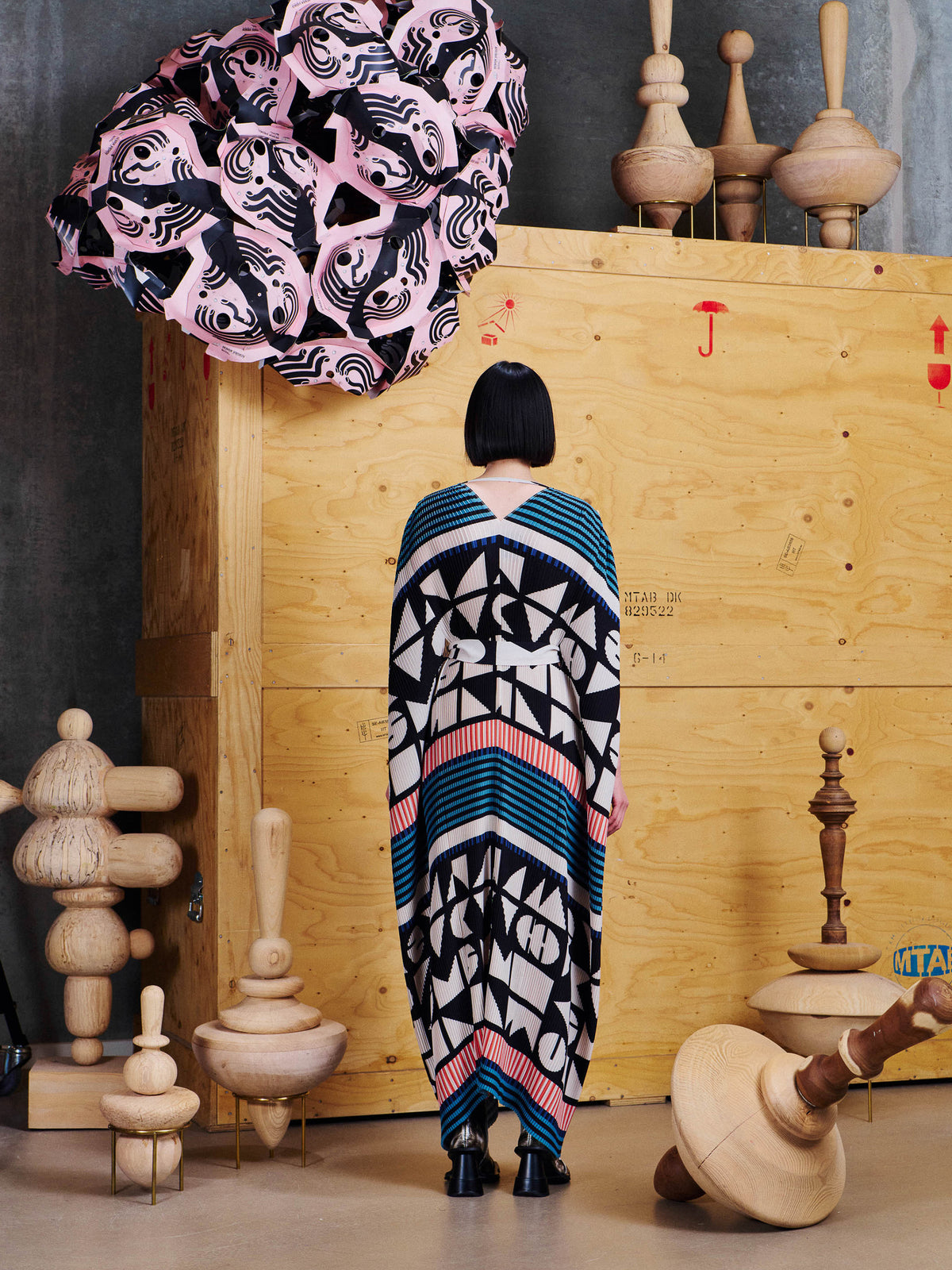 Back view of model wearing Henrik Vibskov Cherry Plisse Kaftan in Vibs In Bobs, showing the V-shaped back neckline, waist tie and graphic pattern.