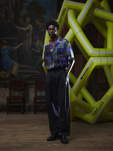 Front full-body view of a male model wearing the Claus Pants in Tropical Black from Henrik Vibskov Spring/Summer 2026 Studio Collection, showing the straight-leg cut, front button closure, and relaxed unisex fit.