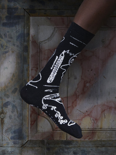Close-up of a leg wearing the Doodle Socks in Black Doodle from Henrik Vibskov Spring/Summer 2026 Studio Collection, highlighting the black base and white doodle-style pattern.