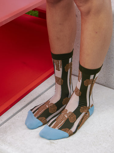 Model wearing Dreamcatcher Socks Femme in Brown Catcher by Henrik Vibskov, tight-fitting striped socks with black and white bands, brown dreamcatcher motif and blue accents, styled on legs, Henrik Vibskov Spring/Summer 2026