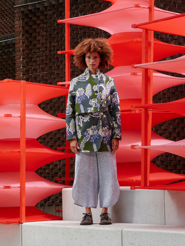 Model wearing Henrik Vibskov Early Evening Coat in Garden of Eeden, shown from the front with high neckline and defined waist tie.