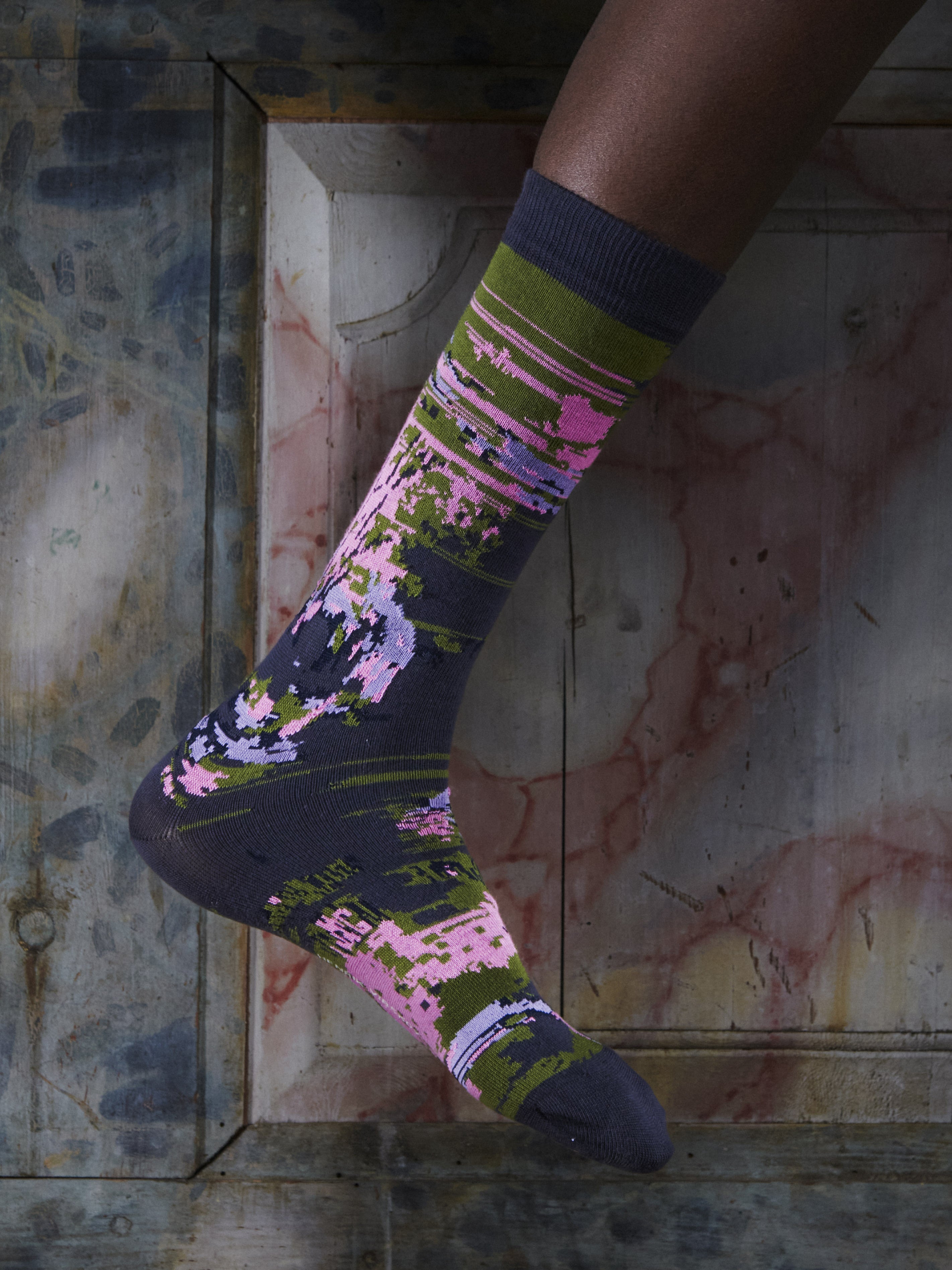 Close-up of a leg wearing the Foxy Socks in Black Foxy from Henrik Vibskov Spring/Summer 2026 Studio Collection, highlighting the black base and multicoloured fox-pattern design.