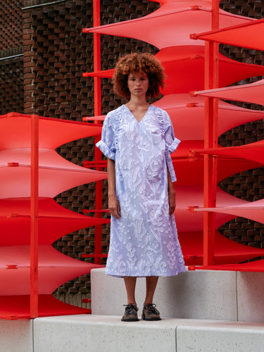 Front view of a model wearing the light blue Insurance Dress with white textured floral pattern, V-neck, and relaxed fit.