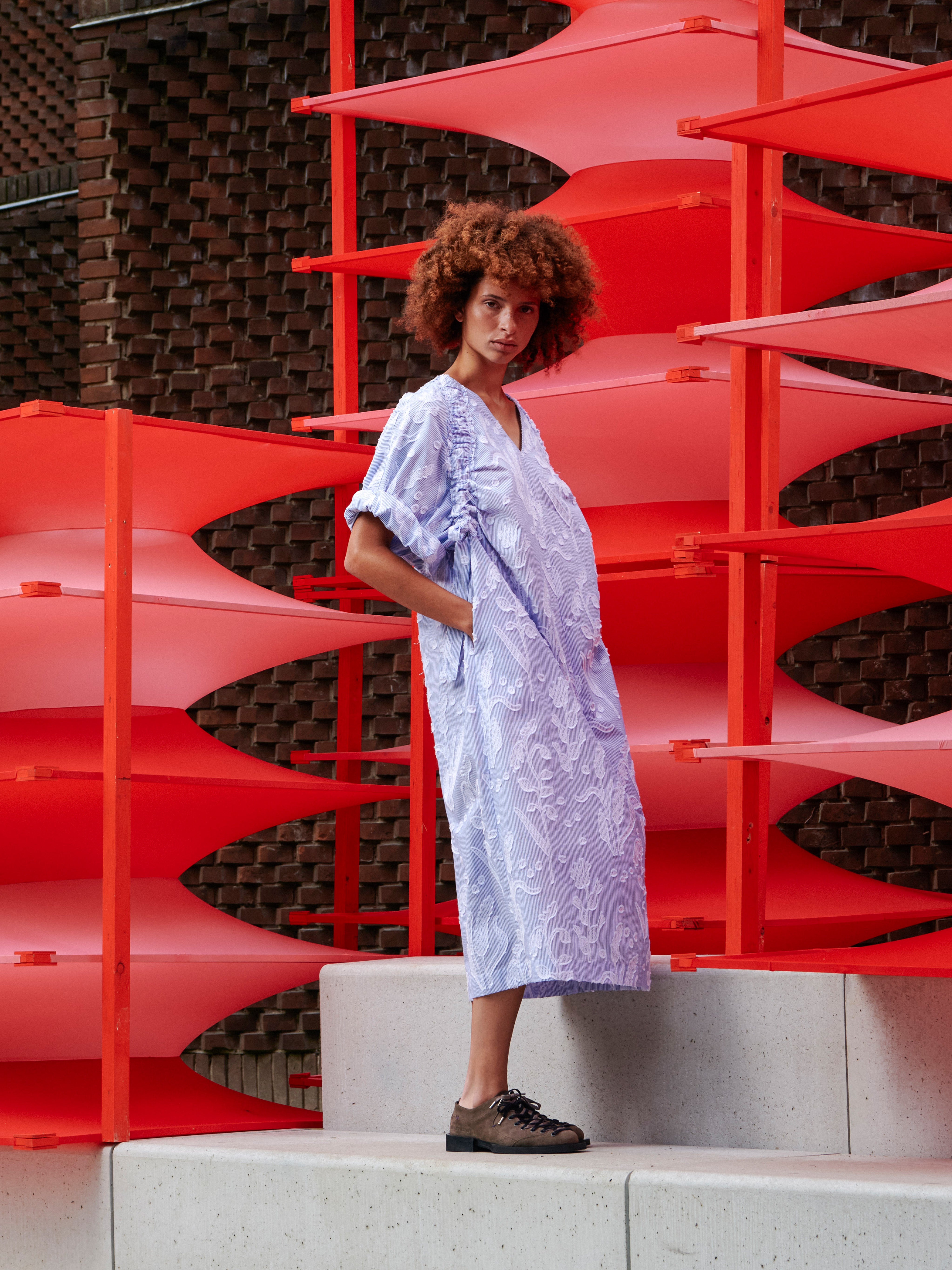 Side view of a model wearing the Insurance Dress, highlighting the loose silhouette and drawstring details on the sleeves.