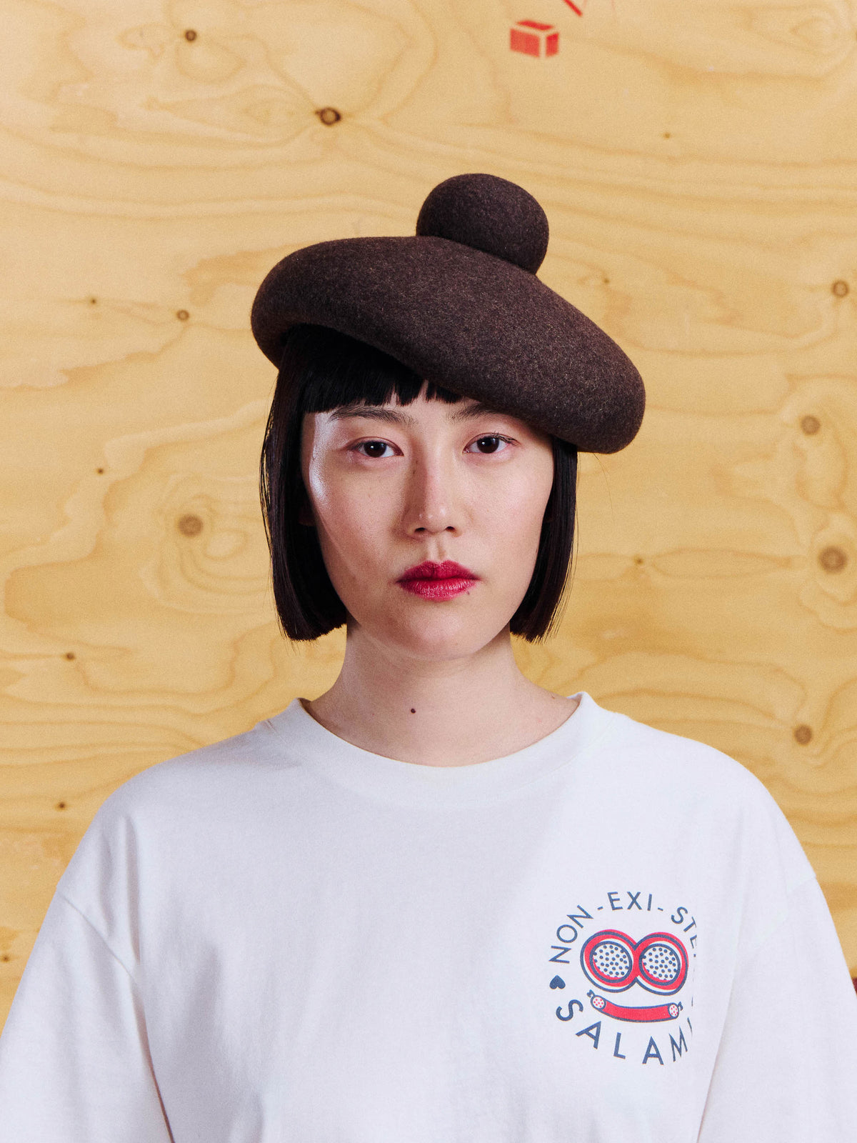 Henrik Vibskov Macaron Hat in Brown worn with a white Salami Tee, showing the rounded silhouette and raised crown detail.