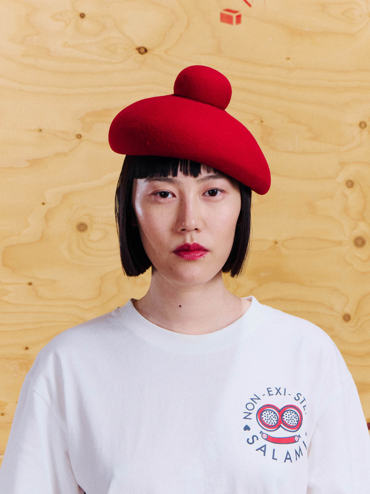 Henrik Vibskov Macaron Hat in Red worn with a white Salami Tee, showing the rounded silhouette and raised crown detail.