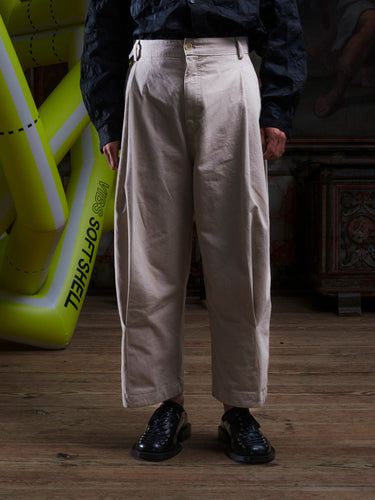 Close-up of the male model wearing the Henrik Vibskov Open Dart Pants in sand beige, front view. The image highlights the pleated front, button fly, and waistband details.