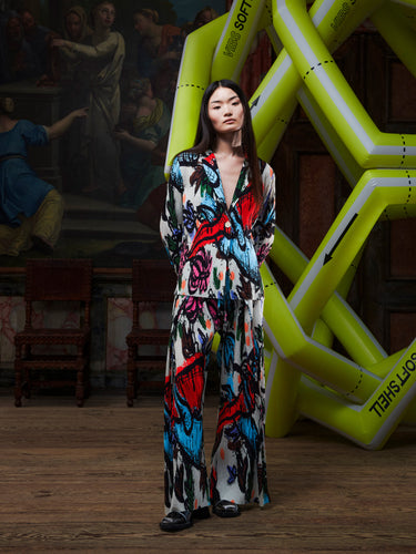 Model wearing the Henrik Vibskov Plissé Blazer in Carrots, front view. The model is 167 cm and wears size S, showing the fitted silhouette, classic blazer collar, and full plissé construction with multicolour root-vegetable print.