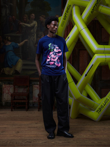 Male model wearing the navy blue t-shirt with a pink rooster illustration by Henrik Vibskov in a setting with an inflatable structure