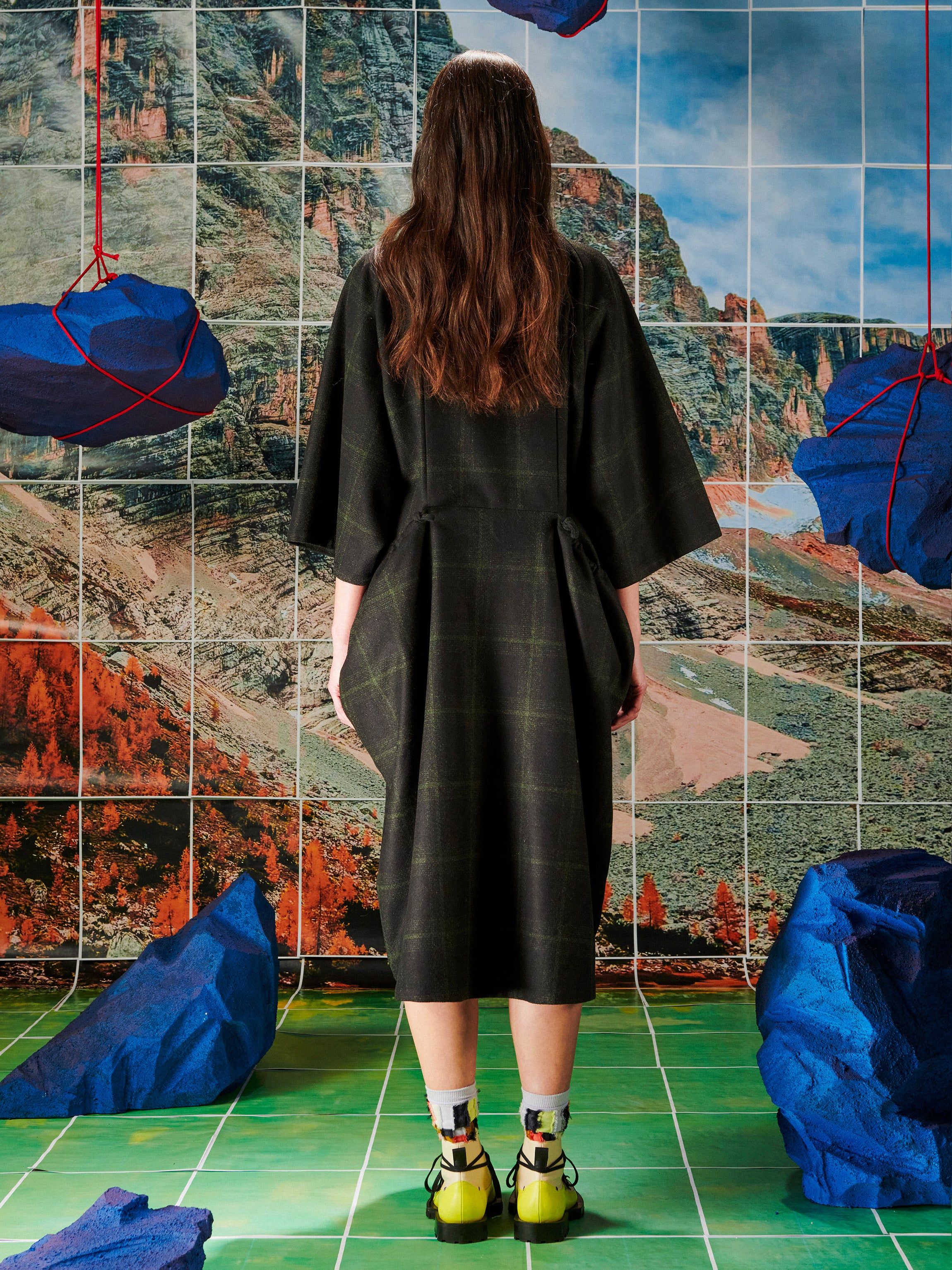 Woman in a black dress standing in front of a colorful abstract wall with blue rocks.
