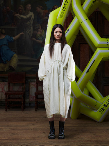 Woman in a beige-grey dress standing in front of a large inflatable yellow sculpture.