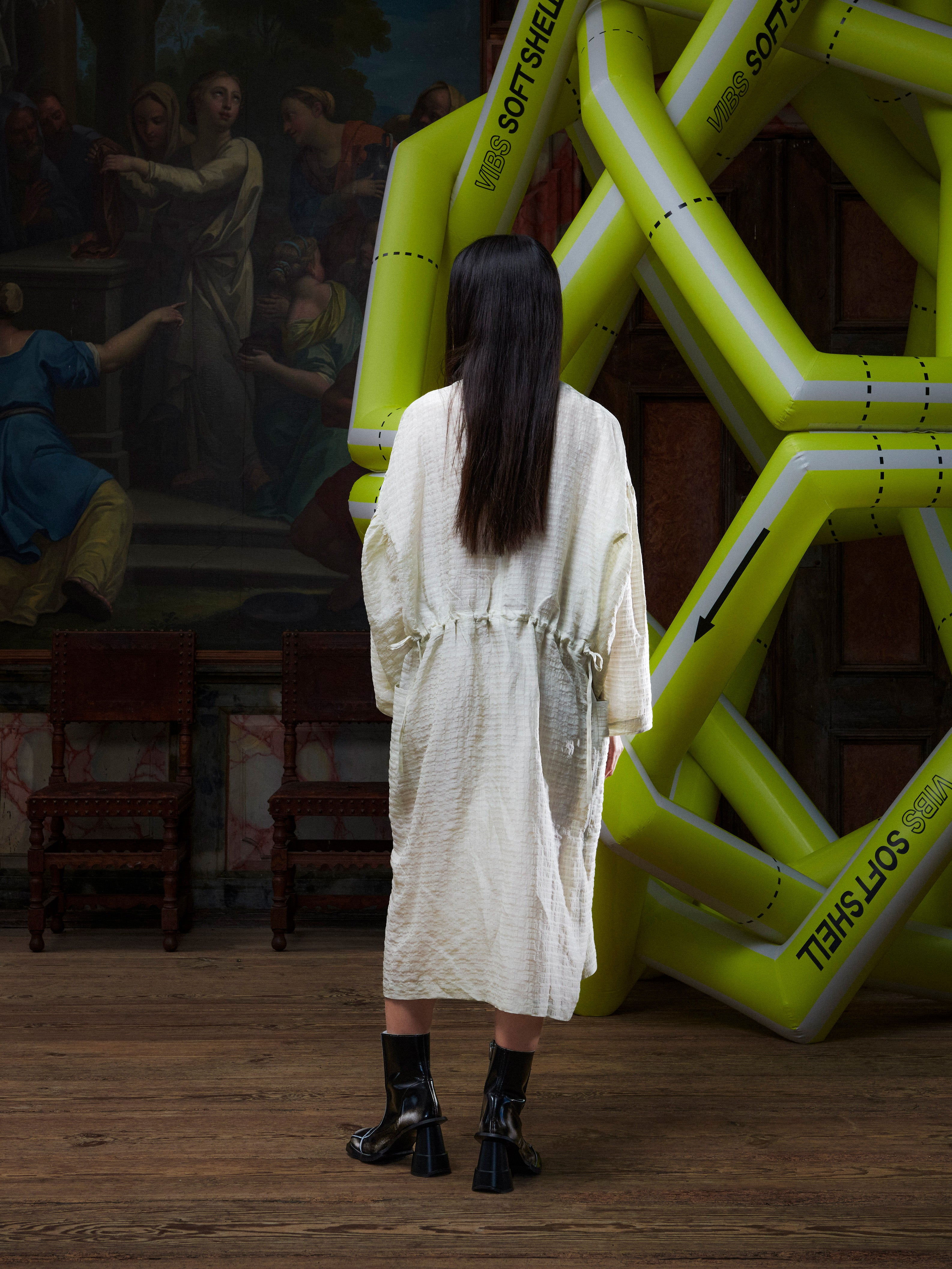 Back view of woman in a beige-grey dress standing in front of a large inflatable yellow sculpture.