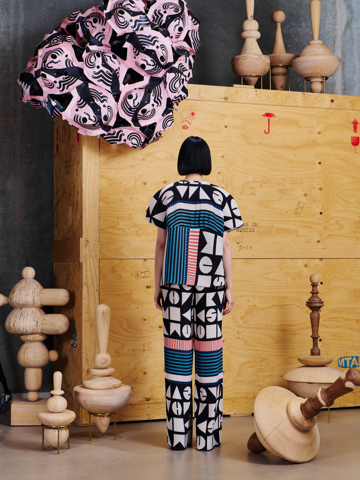 Back view of model wearing Henrik Vibskov Silhouette Plisse Pants in Vibs In Bobs, showing the full-length pleated construction and all-over geometric pattern.