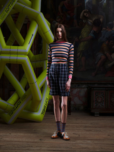 Person wearing a striped sweater and plaid shorts standing in front of a large inflatable object.