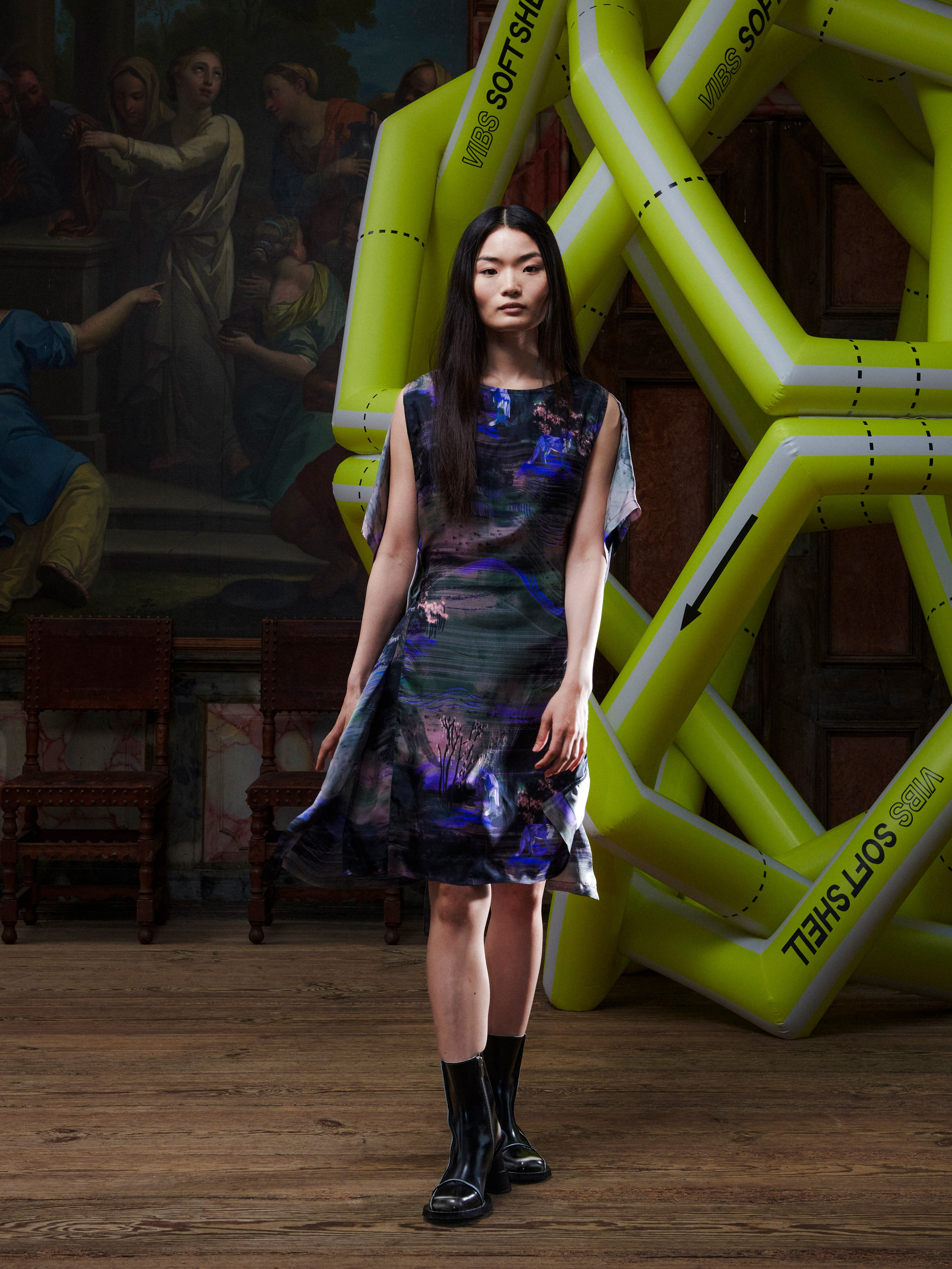 Woman in a patterned dress standing in front of large inflatable letters in an indoor setting.