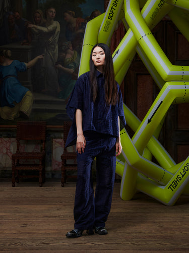 Person in dark blue outfit standing in front of a large inflatable sculpture, in a room with classical painting and furniture.
