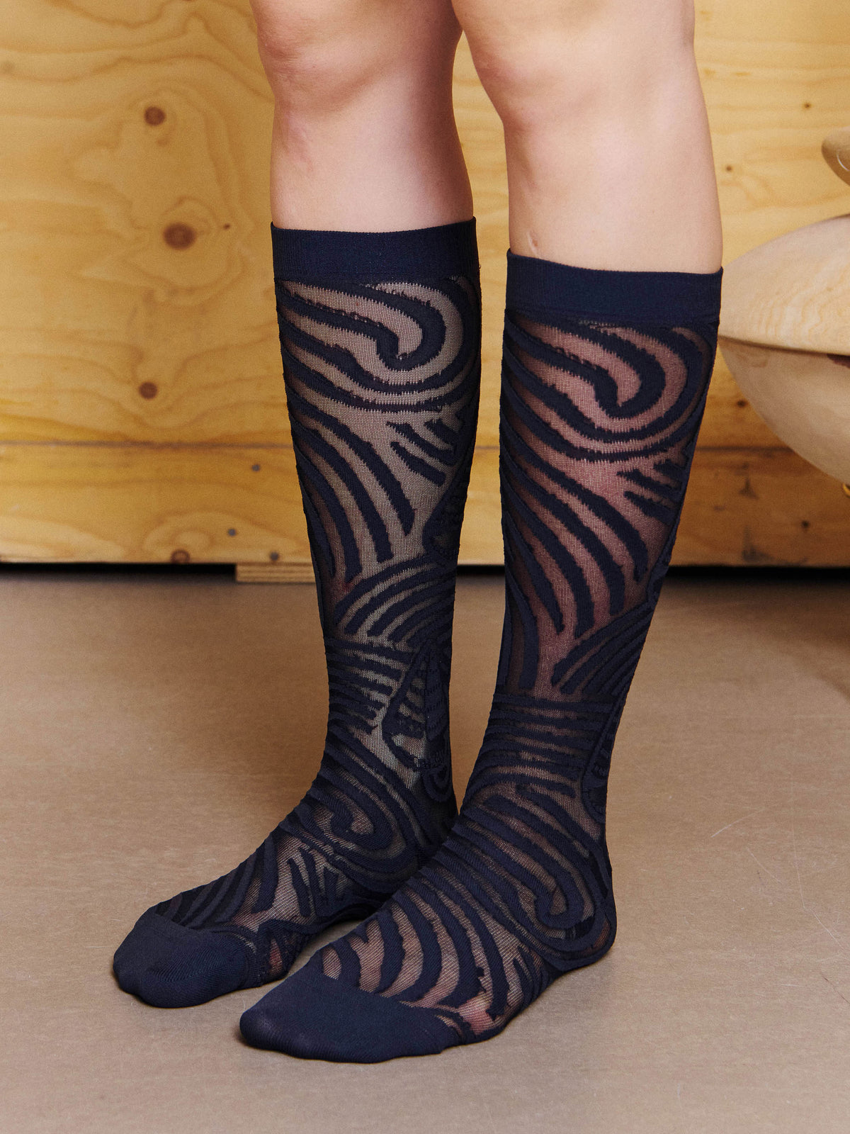 Angled view of model wearing the Henrik Vibskov Stormy Sea Socks in Black Stormy Sea, showing the wave pattern, sailboat motifs and mid-calf fit.