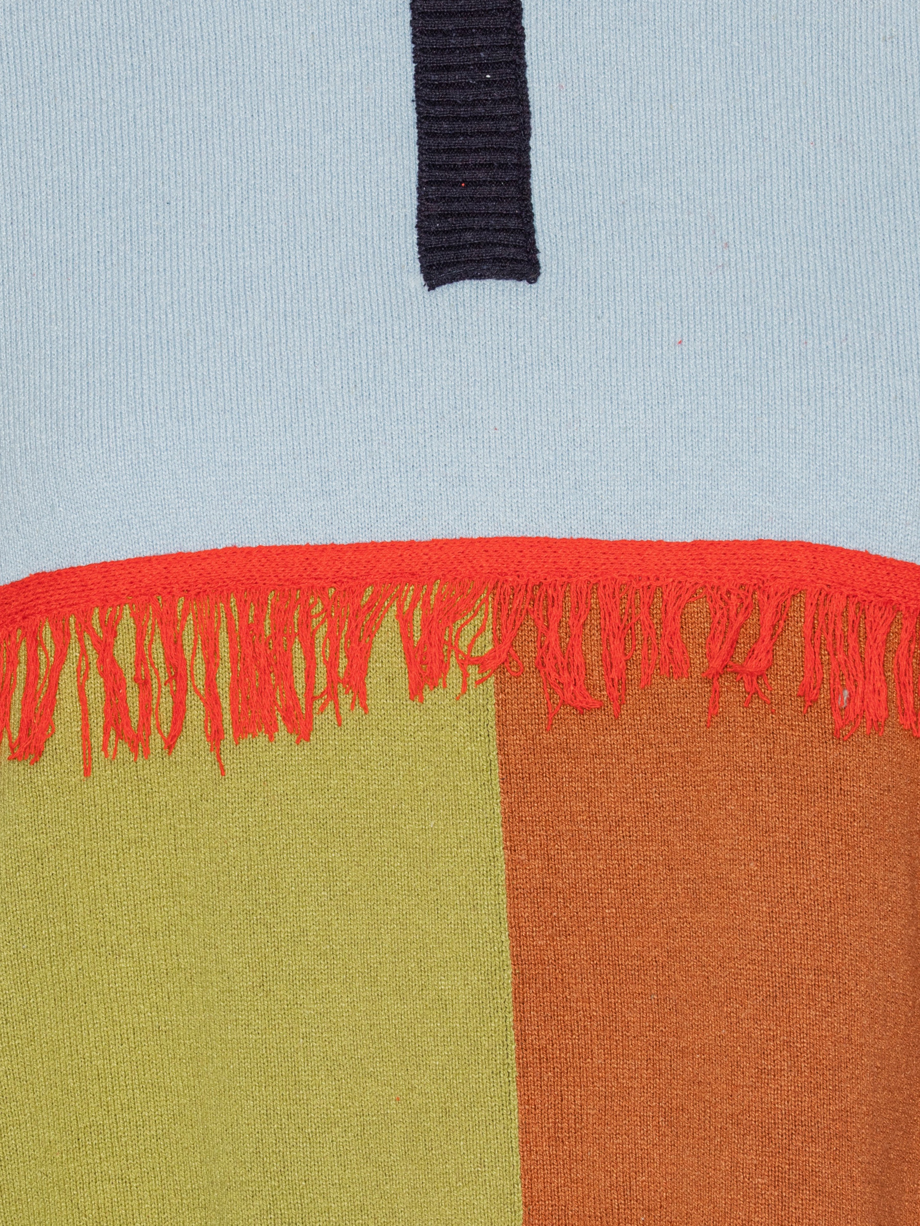 Close up of color-blocked fabric with red fringe on a light blue background