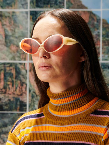 Woman wearing large sunglasses and a striped sweater in front of a colorful abstract wall.