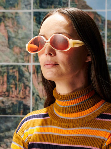 Person wearing yellow sunglasses and a striped sweater in front of a textured wall.