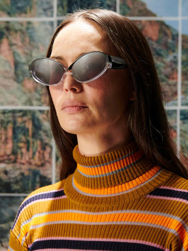 Person wearing sunglasses and a striped sweater in front of a colorful abstract wall.