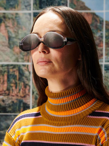 Person wearing sunglasses and a striped sweater in front of a scenic background