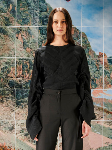 Woman wearing a pleated blouse with adjustable drawstring sleeves from Henrik Vibskov on a mountain tile landscape