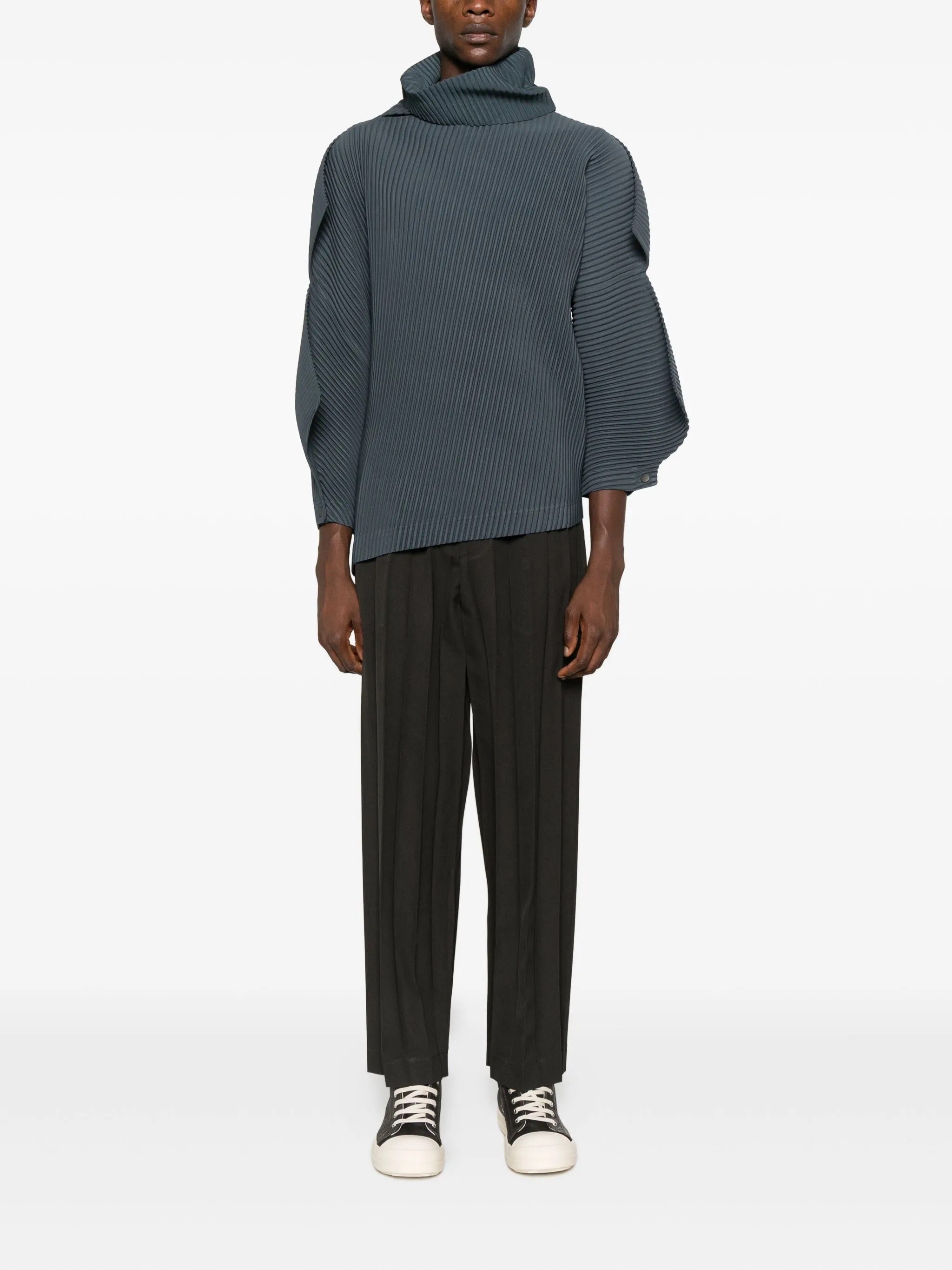 Person wearing a teal sweater and dark brown pants on a white background