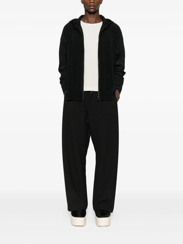Person wearing a black plissé tracksuit with a white shirt underneath on a white background