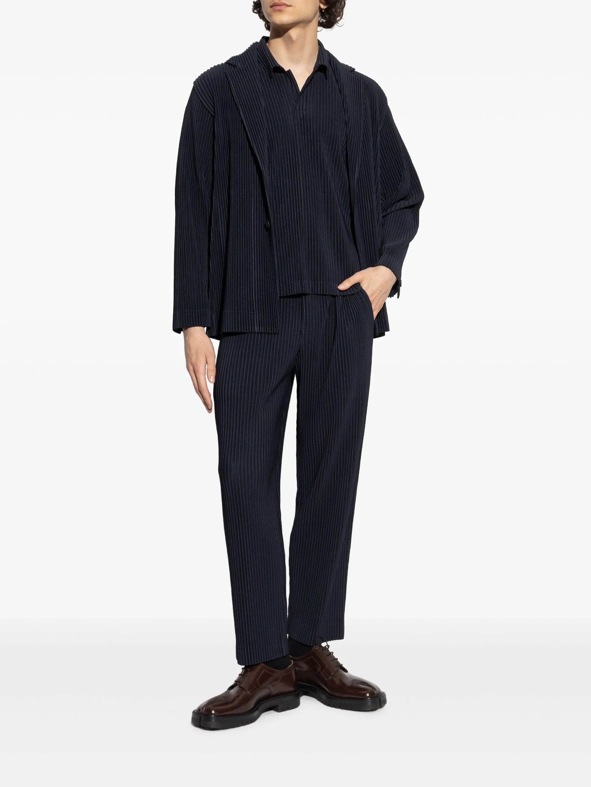 Person wearing a dark blue outfit from Homme Plissé Issey Miyake with a white background