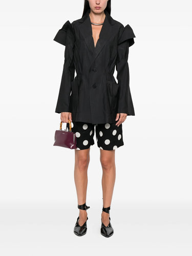 Person wearing a black blazer and polka dot shorts with a white background