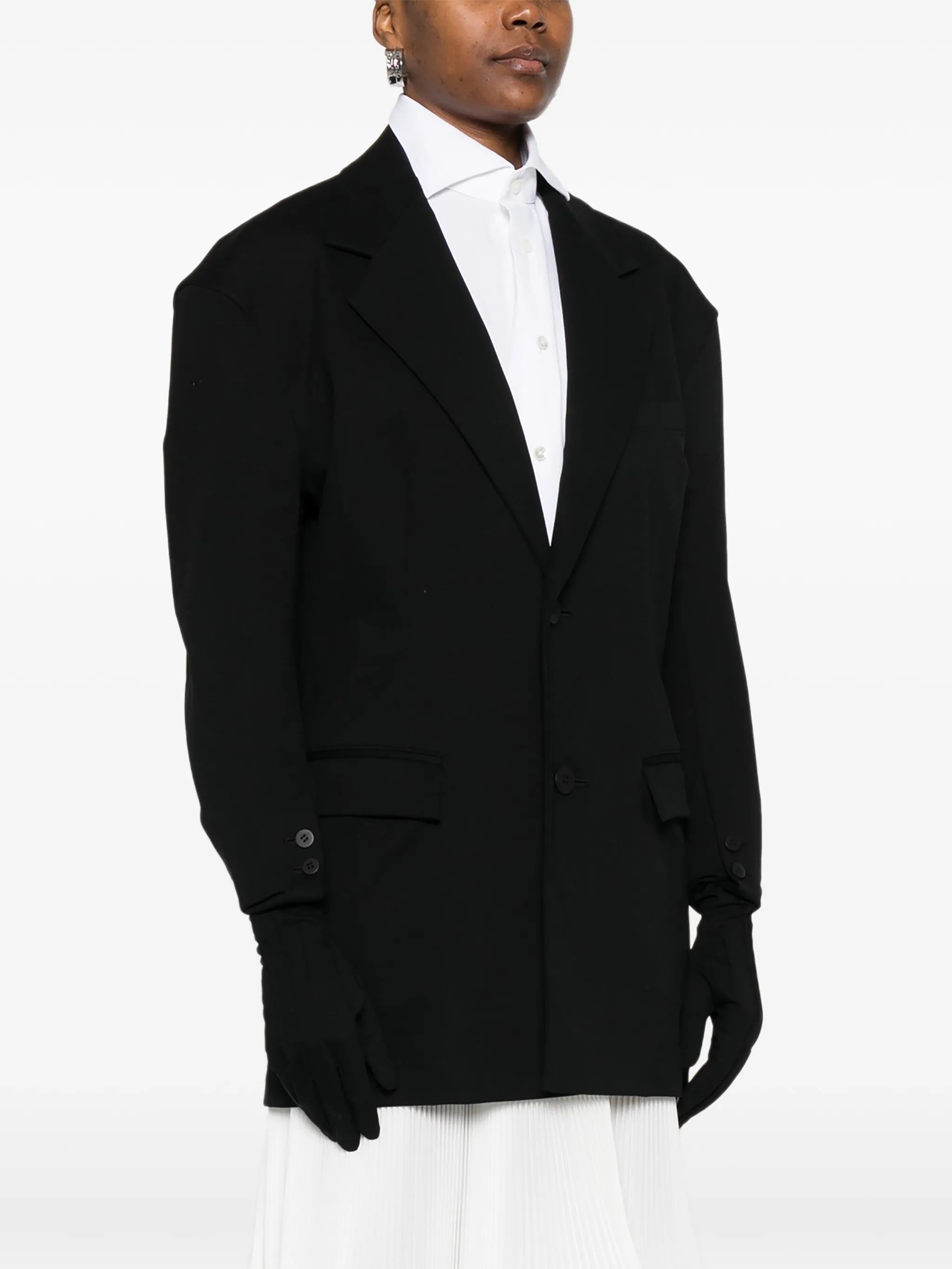 Close-up of model wearing the black blazer with gloves attached to sleeves from Issey Miyake on a white background